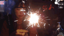 a woman is holding a sparkler in front of her face and the number 5 is written in red