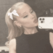 ariana grande is taking a selfie in front of a mirror with a bow in her hair .