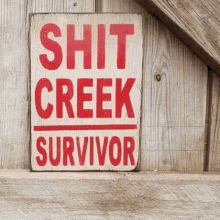 a sign on a wooden wall that says `` shit creek survivor '' in red letters .