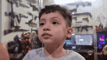 a young boy is sitting in front of a computer in a room with a lot of guns on the wall .