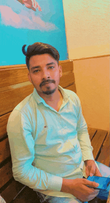 a man in a green shirt is sitting on a wooden bench holding a cell phone