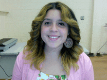 a woman wearing a pink cardigan and earrings smiles in front of an epson printer