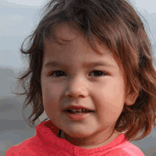 a close up of a little girl 's face with a pink sweater on