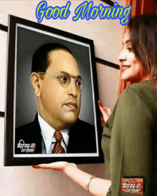 a woman is holding a framed picture of a man with glasses and the words good morning on the bottom