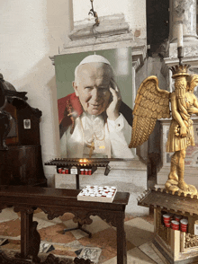 a picture of pope john paul ii hangs above a candle holder in a church