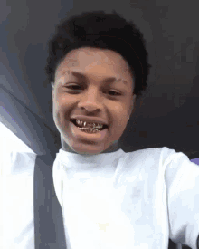 a young man wearing a white shirt and gold grills is taking a selfie .