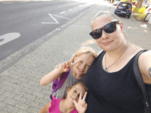 a woman wearing sunglasses and a black tank top poses with two young girls