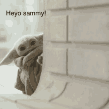 a baby yoda is peeking out from behind a brick wall and saying heyo sammy .