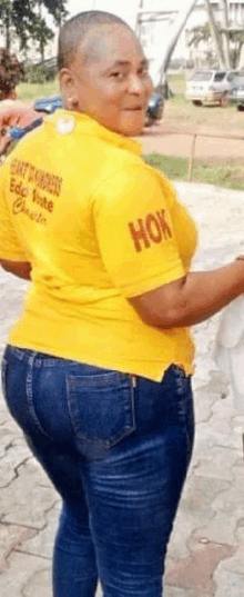 a woman with a shaved head is wearing a yellow shirt and blue jeans .