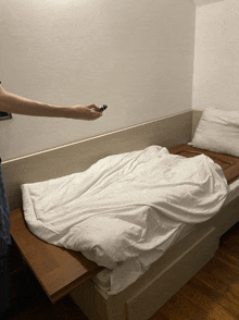 a person holding a remote control in front of a bed with white sheets