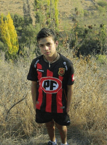 a young boy wearing a black and red pf shirt stands in a field