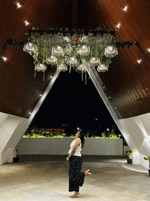 a woman stands under a chandelier with flowers hanging from the ceiling