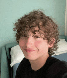 a young boy with curly hair wearing a black shirt smiles for the camera