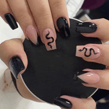 a woman 's nails are painted in black and pink with a snake design .