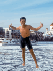 a shirtless man stands in a body of water with a boat in the background