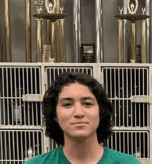 a young man wearing a green shirt is standing in front of a row of trophies .