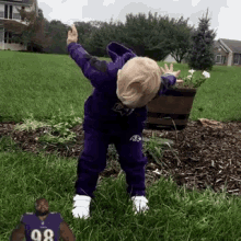 a little boy in a purple outfit is standing in the grass with a picture of a man in a number 98 jersey