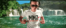 a man wearing a mmz t-shirt is running in front of a waterfall