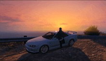 a person standing next to a white car with the sun setting in the background