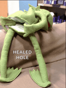 a stuffed kermit frog is laying on a couch with the words healed hole above it