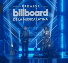 a man and a woman are standing on a stage in front of a sign that says billboard de la musica latina