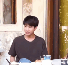 a young man is sitting at a table with a plate of food and a cup with the word ice cream on it