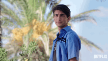 a man in a blue shirt is standing in front of a palm tree with a netflix logo behind him