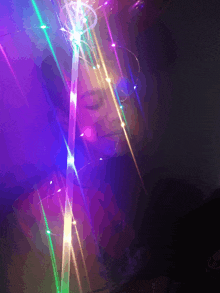 a woman is surrounded by a rainbow of lights including purple and green