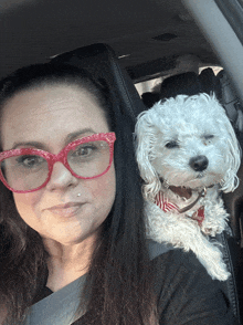 a woman wearing red glasses holds a small white dog