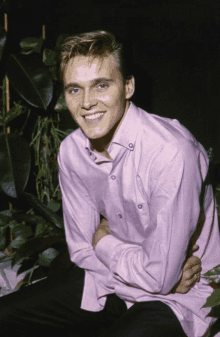 a young man wearing a pink shirt is smiling for the camera