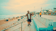 a man in a colorful shirt and shorts stands on a beach