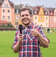 a man in a plaid shirt is holding a microphone and giving a thumbs up sign