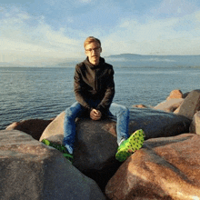 a young man is sitting on a large rock near the ocean .