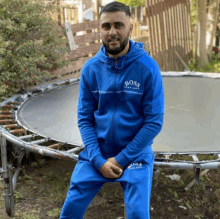 a man wearing a blue boss tracksuit is sitting in front of a trampoline