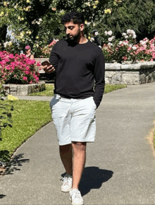 a man in a black sweater and white shorts is walking down a sidewalk looking at his phone