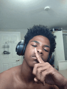 a shirtless man wearing headphones holds his finger to his mouth