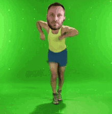 a man in a yellow tank top and blue shorts is jumping in the air on a green screen .