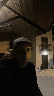 a man wearing a flat cap stands in front of a building at night