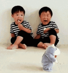 two young boys are sitting on the floor eating ice cream while a stuffed animal is standing between them .