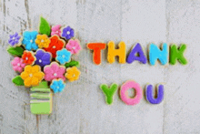 a bouquet of flowers in a vase with the words `` thank you '' written on a wooden surface .