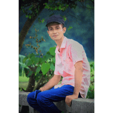 a young man in a pink shirt and black hat sits on a wall