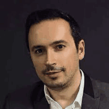 a man in a suit and white shirt is standing in front of a black background .