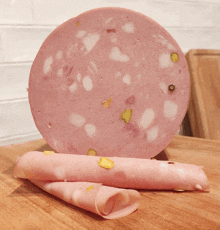 a slice of pink sausage with pistachios on a wooden cutting board