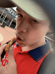 a young man wearing a hat and a red shirt eating a cookie