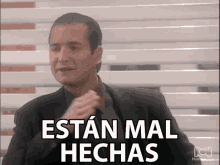 a man in a suit adjusts his tie with the words estan mal hechas above him