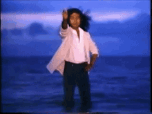 a woman in a white jacket and black pants is dancing on a beach