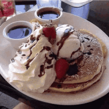 a person is holding a plate of pancakes with whipped cream , ice cream , strawberries and chocolate sauce .