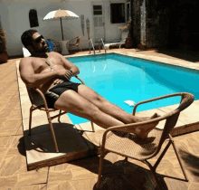 a shirtless man is laying in a chair near a swimming pool