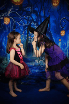 a little girl in a witch costume holds her hand to her mouth