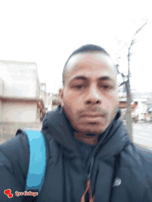 a man wearing a black jacket and a blue backpack is taking a selfie with the words love collage above his head